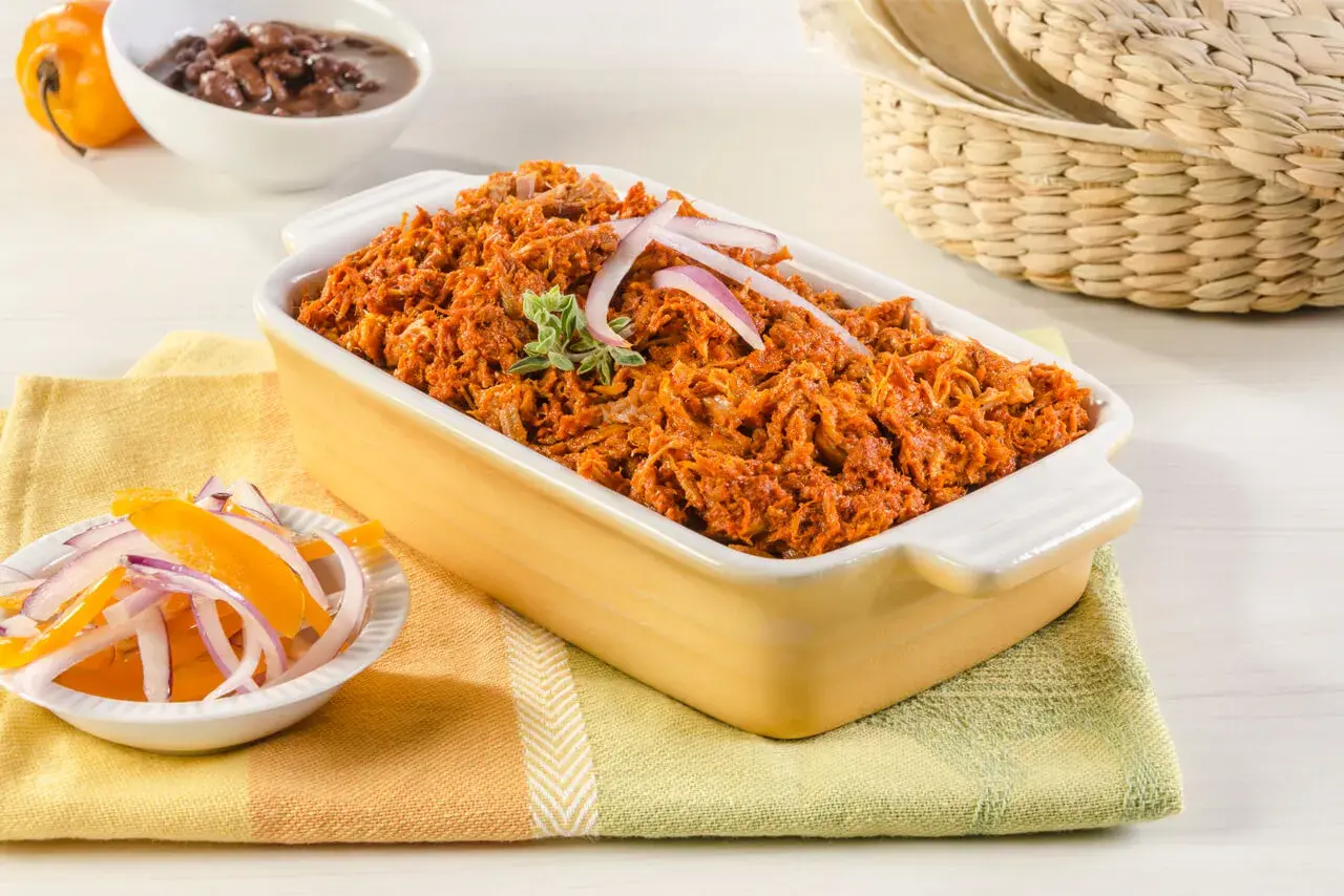 Cochinita pibil, un platillo yucateco de cerdo deshebrado en achiote, servido con cebolla morada y naranja.