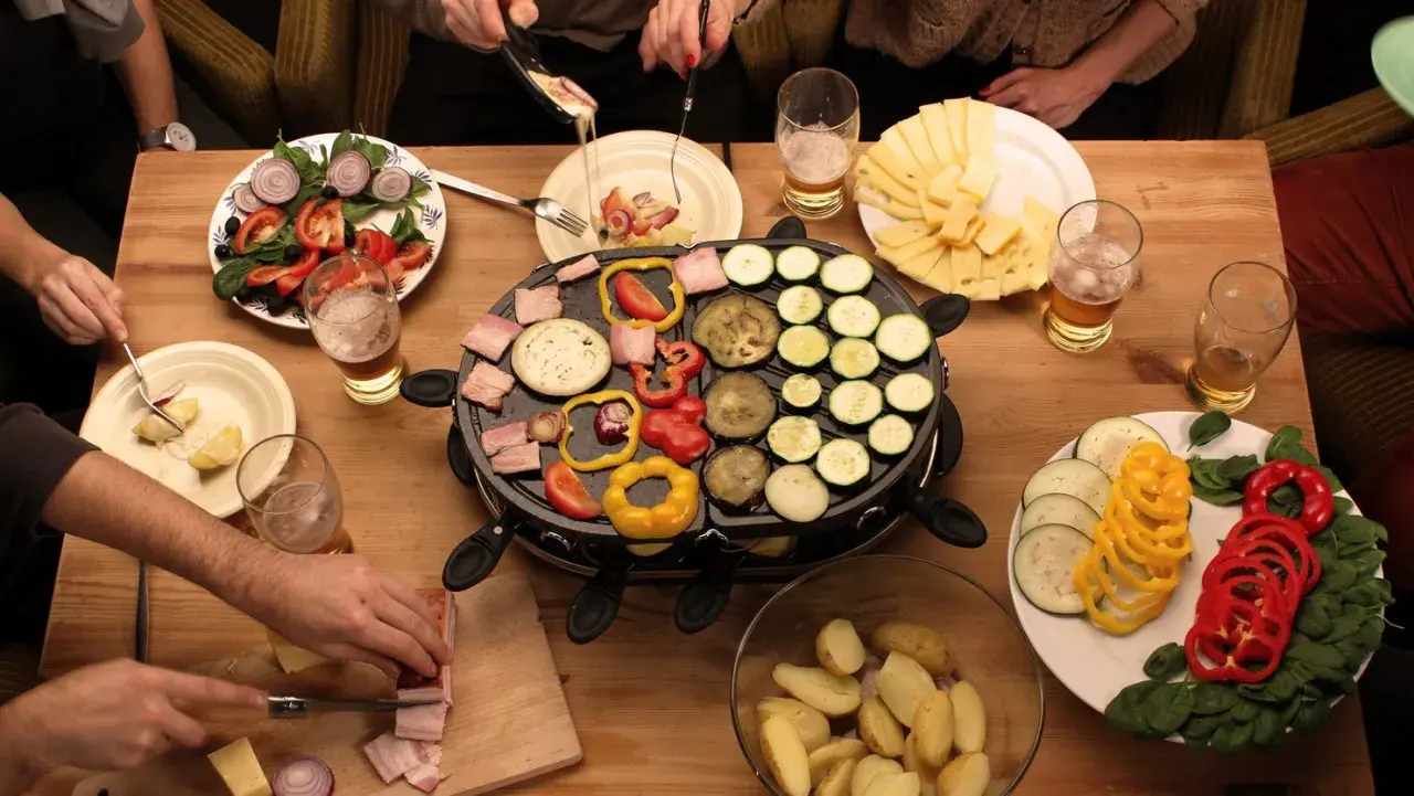 Mesa con raclette, queso, verduras y patatas. ¡Ideas raclette para una cena divertida!