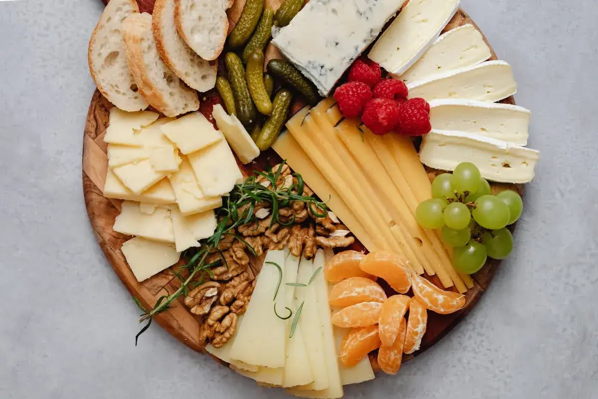 Tabla de quesos como hacerla: variedad de quesos, uvas, frutos rojos, nueces, pepinillos y pan.