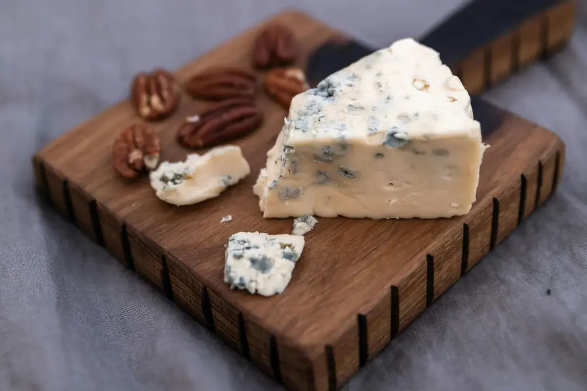 Un trozo de queso azul, ideal para la flora intestinal, reposa sobre una tabla de madera junto a nueces pecanas.