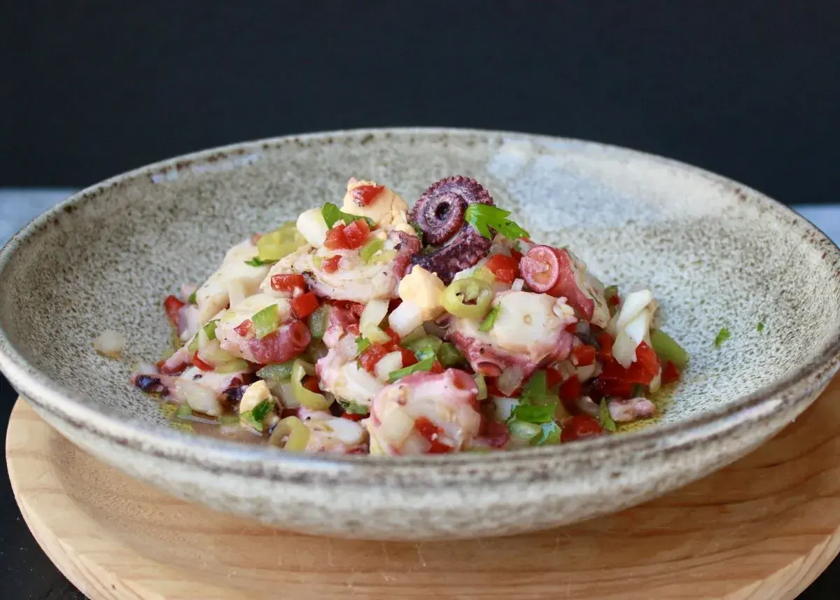 Un refrescante salpicón de pulpo con pimientos, cebolla y aceitunas, servido en un cuenco rústico.