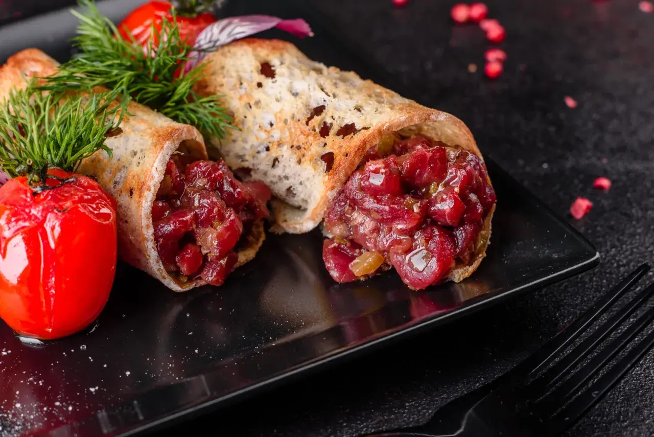 Delicioso steak tartar servido en pan tostado, acompañado de tomates cherry asados y eneldo fresco.