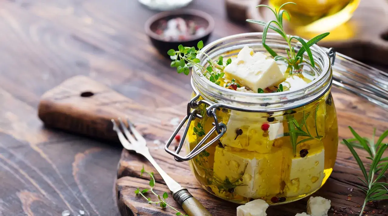 Queso en aceite de oliva, con hierbas aromáticas y granos de pimienta, listo para disfrutar.