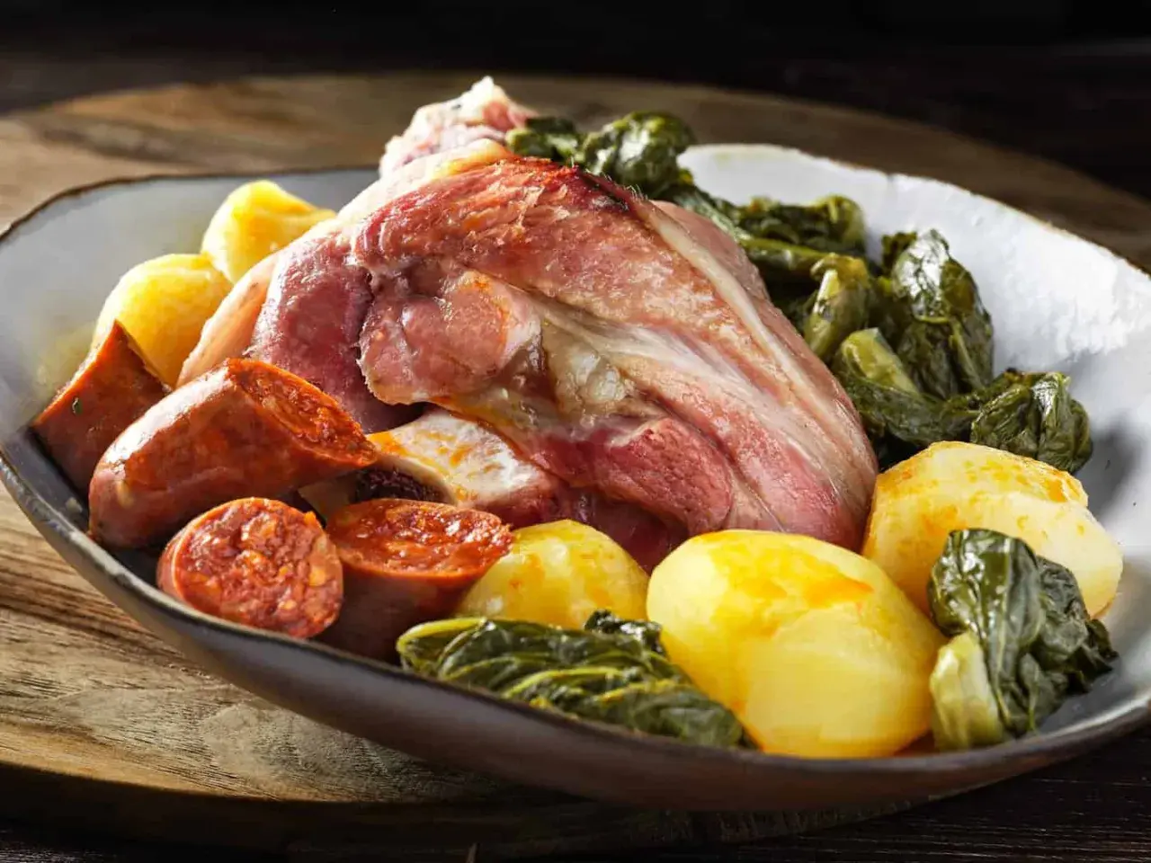 Un plato generoso de lacon con grelos, acompañado de chorizo y patatas cocidas, listo para ser disfrutado.
