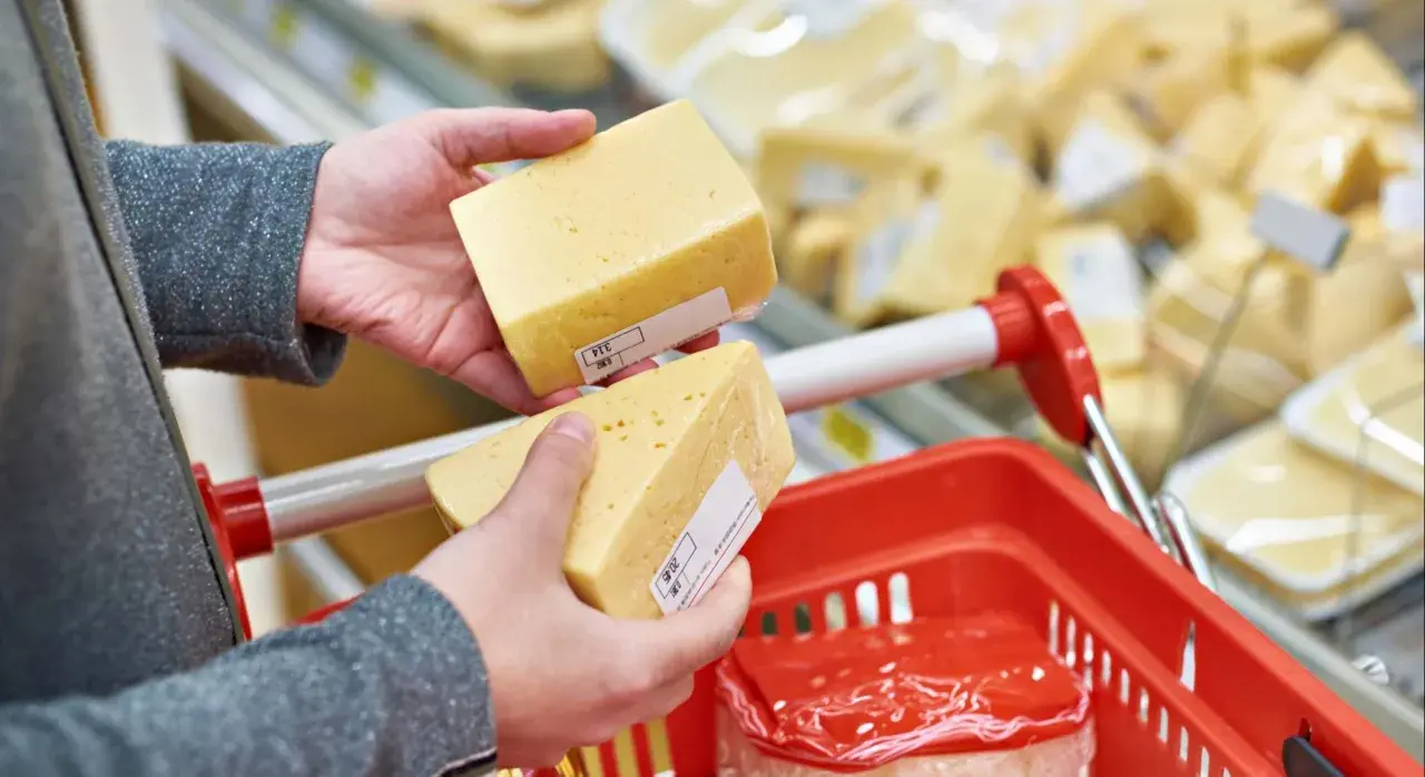 Manos sostienen trozos de queso cheddar, buscando opciones sin lactosa en el supermercado.