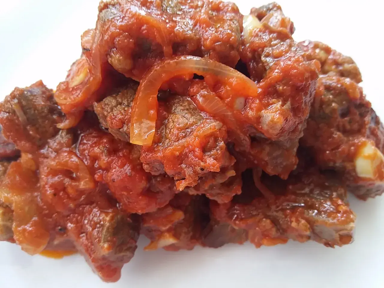 Un plato humeante de carne con tomate y cebolla, cocinado a fuego lento hasta que la carne esté tierna y la salsa espesa.