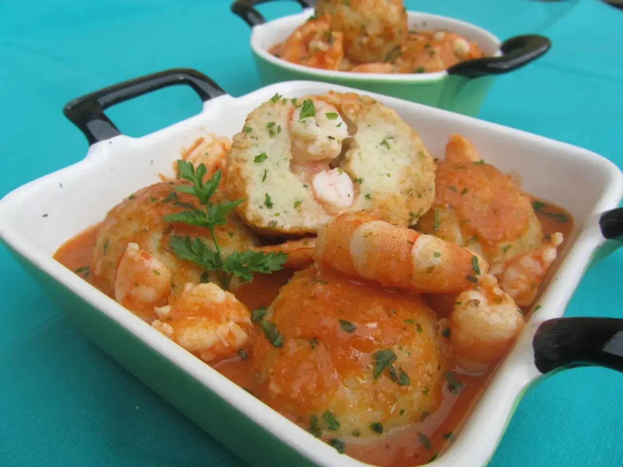 Deliciosas albóndigas de rape con gambas en salsa de tomate, adornadas con perejil fresco.