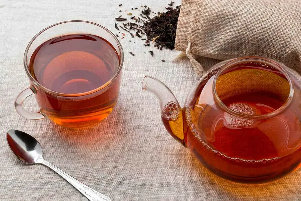 Una taza y tetera de té negro, con hojas secas esparcidas. ¿A que sabe el té negro? A un sabor robusto y reconfortante.