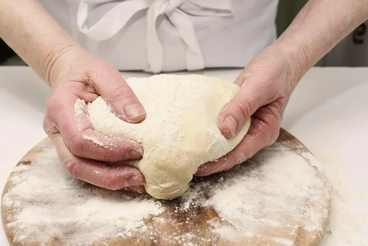 Manos amasando masa con harina, preparando diferentes tipos de levadura para panadería.