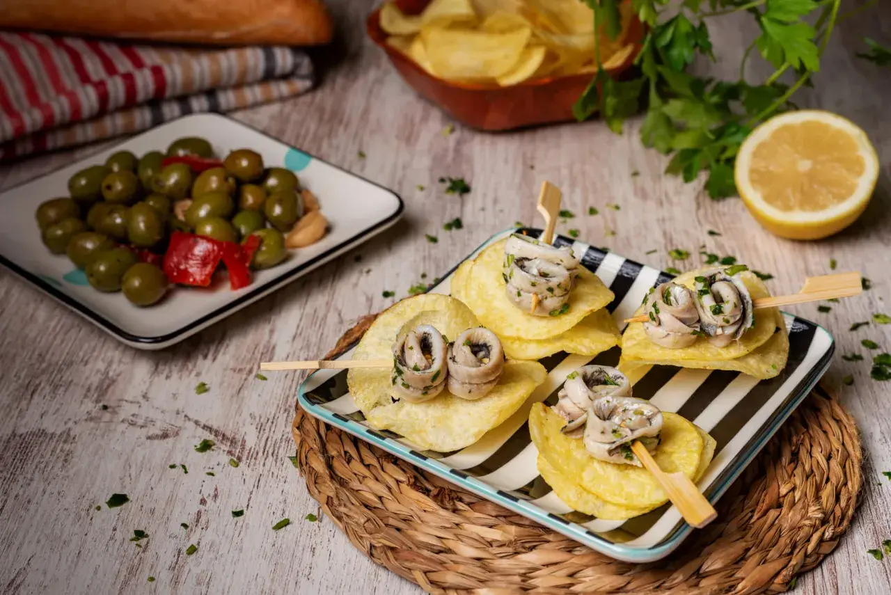 Deliciosas recetas con anchoas: pinchos de anchoas enrolladas sobre patatas fritas, acompañadas de aceitunas y limón.