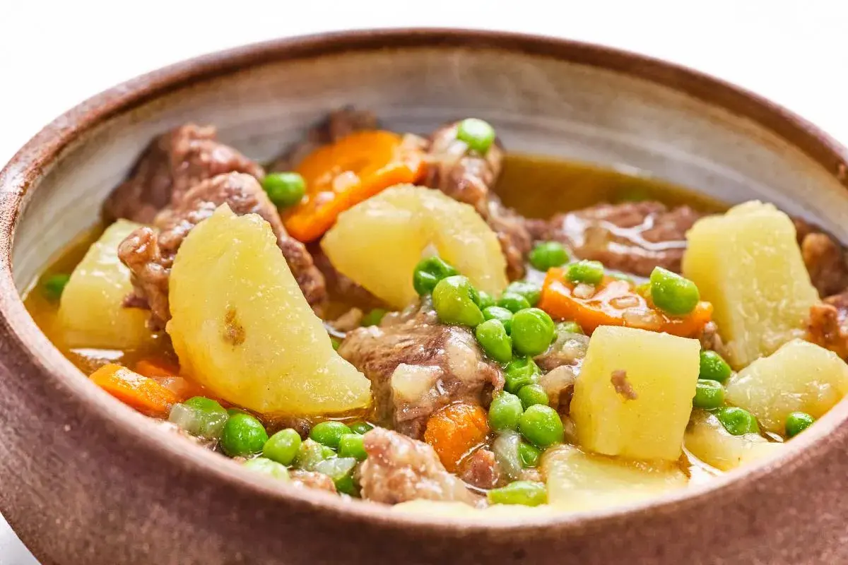 Un reconfortante ragú de ternera con patatas, zanahorias y guisantes en un cuenco de barro.