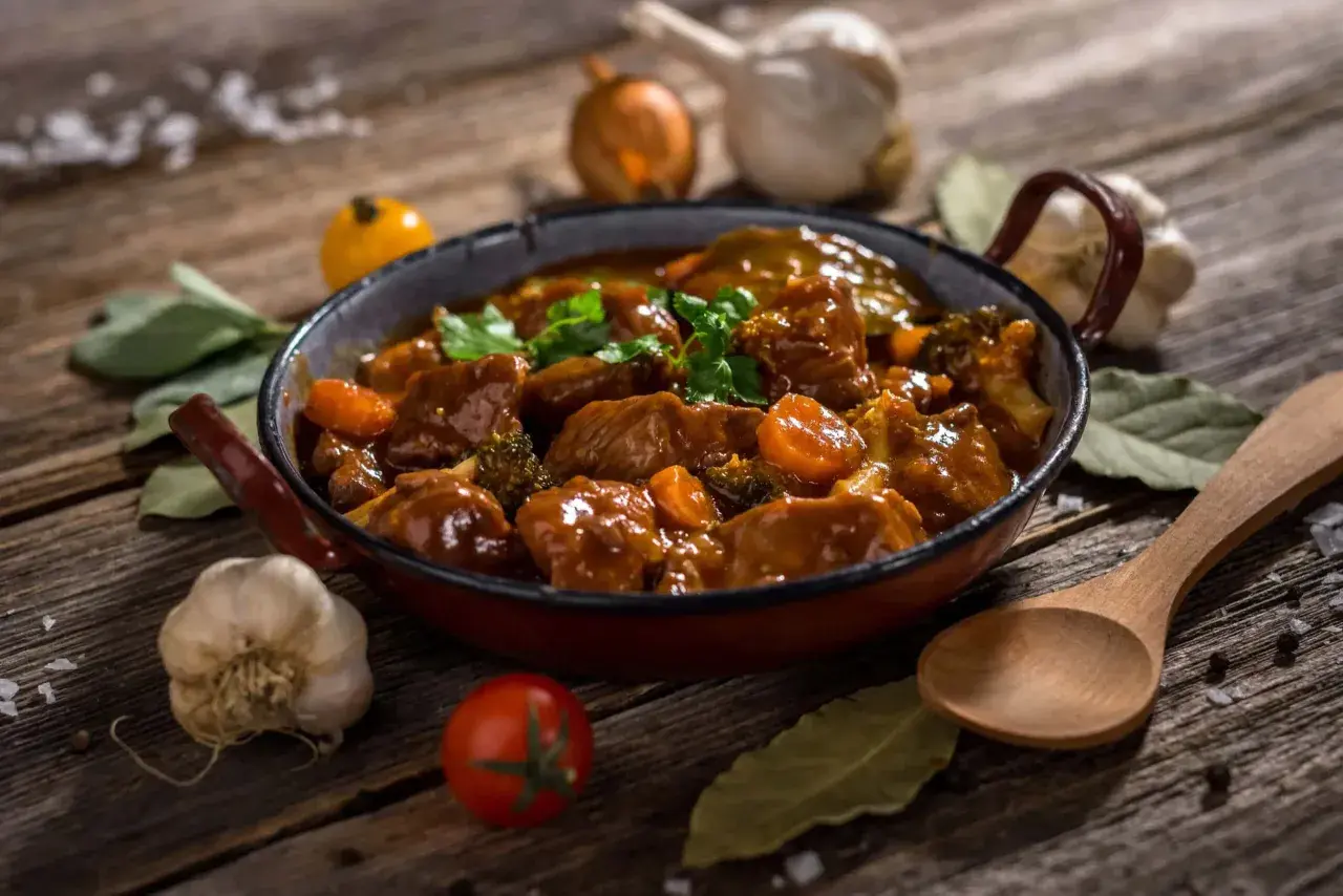 Un delicioso ragú de carne con zanahorias y brócoli en una sartén, acompañado de ajo, cebolla y hierbas.