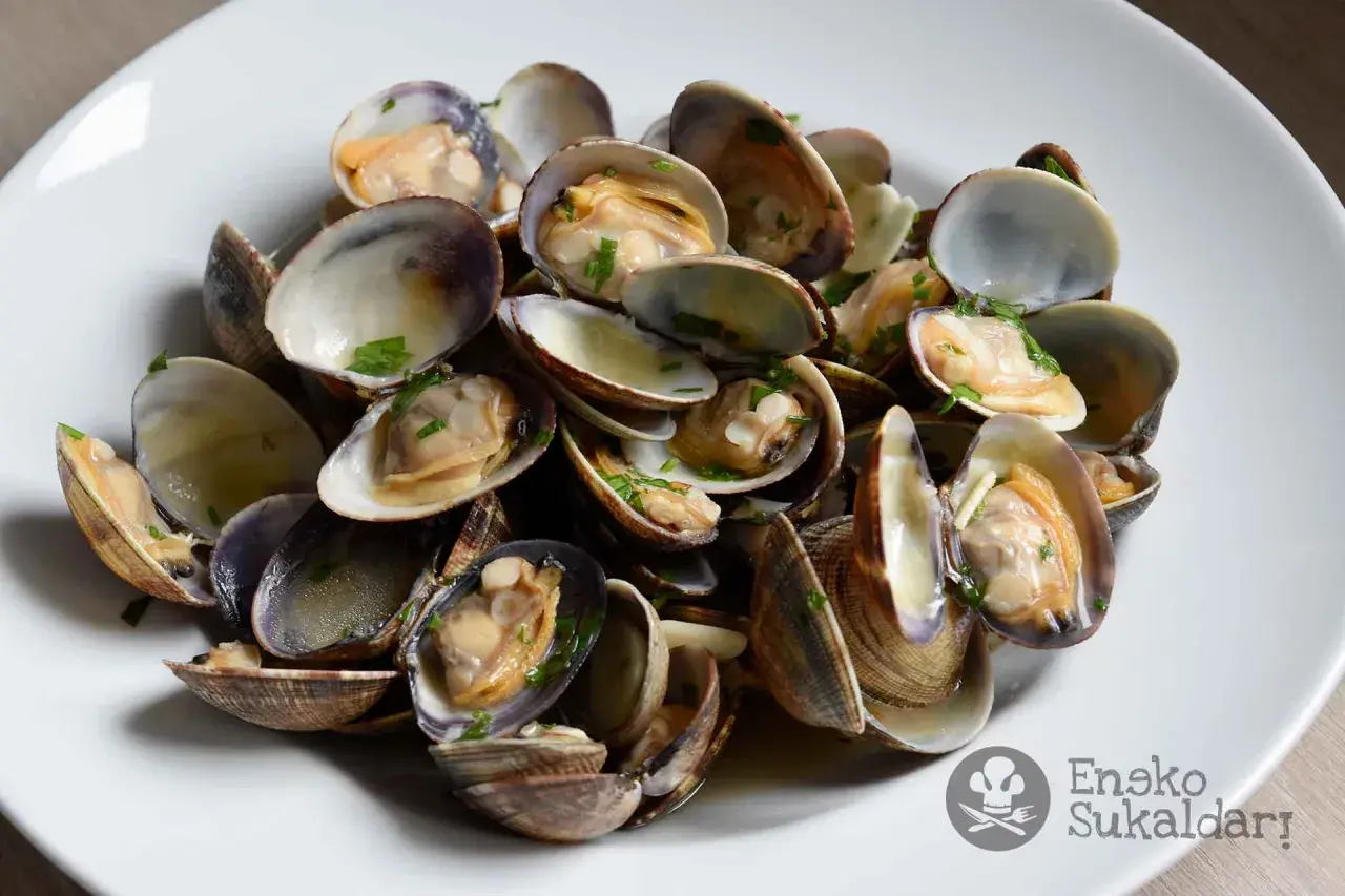 Un plato de almejas a la marinera, recién cocinadas y espolvoreadas con perejil picado.