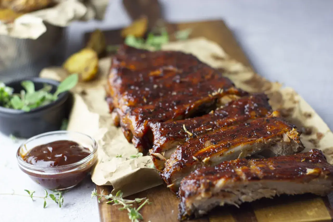 Costillas de cerdo al horno, jugosas y glaseadas, servidas con salsa barbacoa y hierbas frescas. ¡Un festín irresistible!