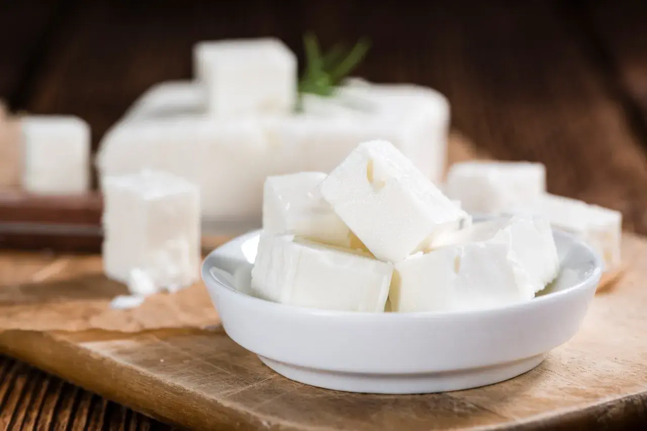 Cubos de queso blanco en un cuenco, con un bloque de queso de leche cruda al fondo. El queso de leche cruda puede presentar peligros.