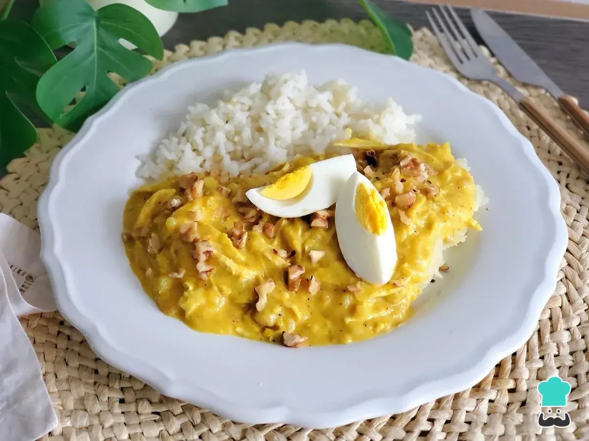Un plato de aji de pollo cremoso con arroz blanco, huevo duro y nueces picadas.