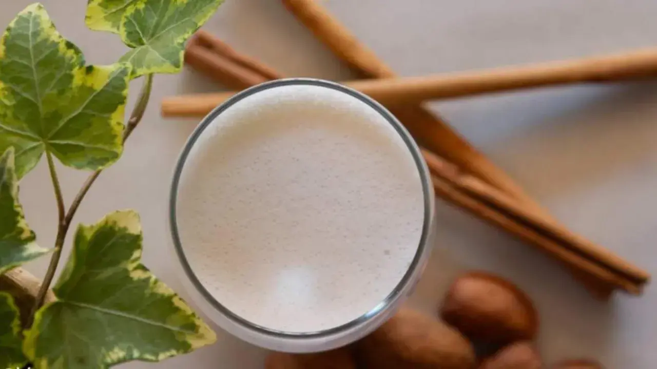Un vaso de leche espumosa, canela y hojas verdes, recordatorio de los beneficios de la leche de vaca para una vida saludable.