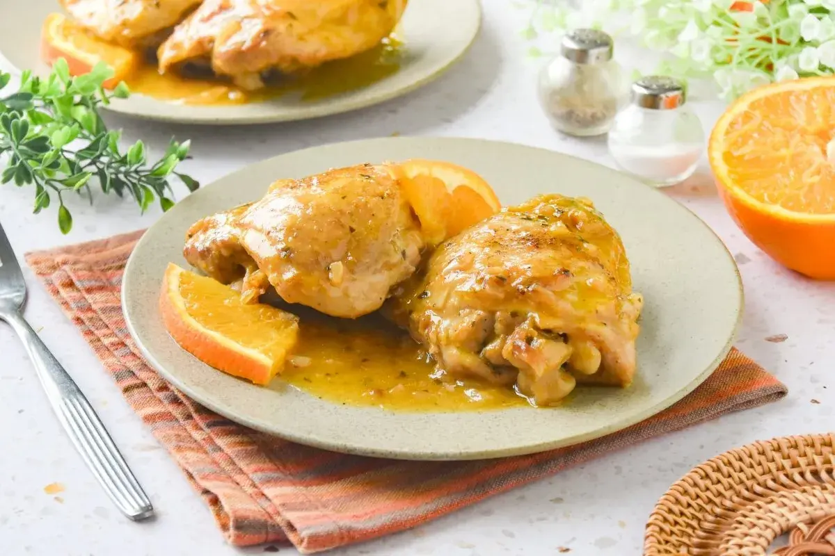 Dos jugosas piezas de pollo a la naranja, bañadas en su salsa y decoradas con gajos de naranja fresca. Un plato delicioso y aromático.