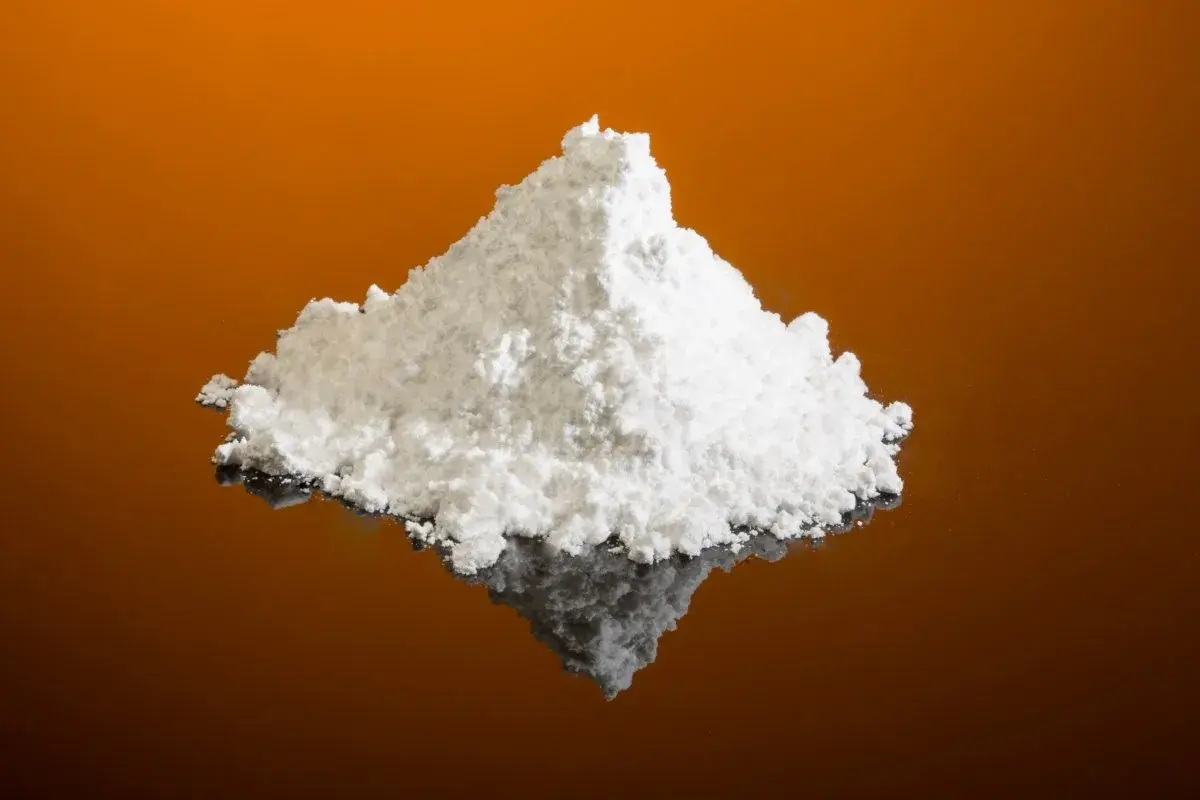 Montículo de polvo blanco fino, que es el cremor tártaro, sobre una superficie reflectante naranja.