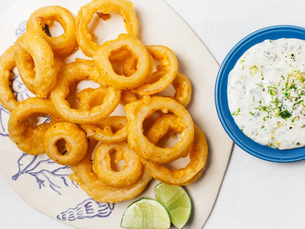 Crujientes aros de cebolla dorados, servidos con una cremosa salsa y gajos de lima. ¡Un aperitivo irresistible!