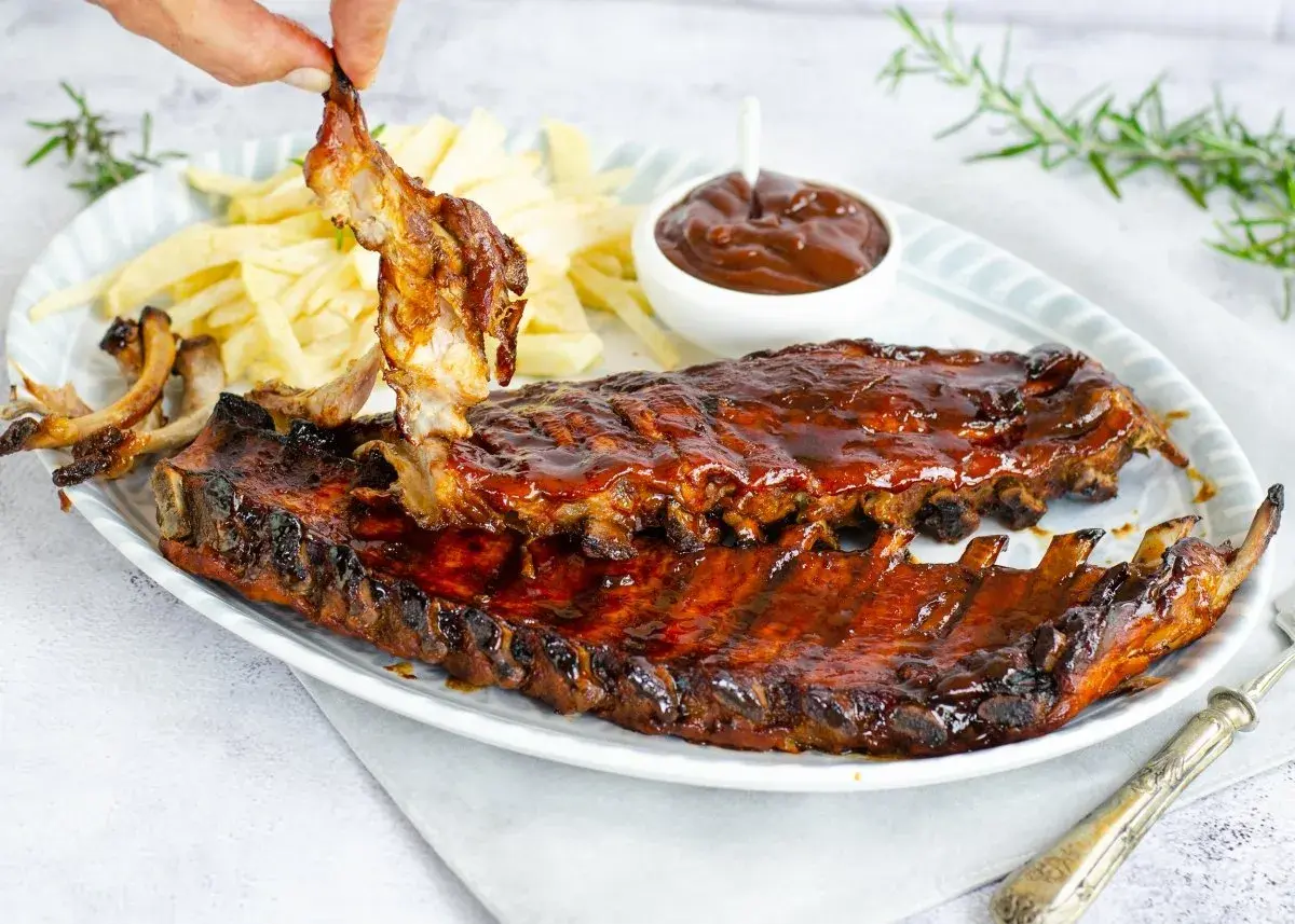 Costillas a la barbacoa jugosas y glaseadas, servidas con patatas fritas y salsa barbacoa. ¡Un festín para los sentidos!
