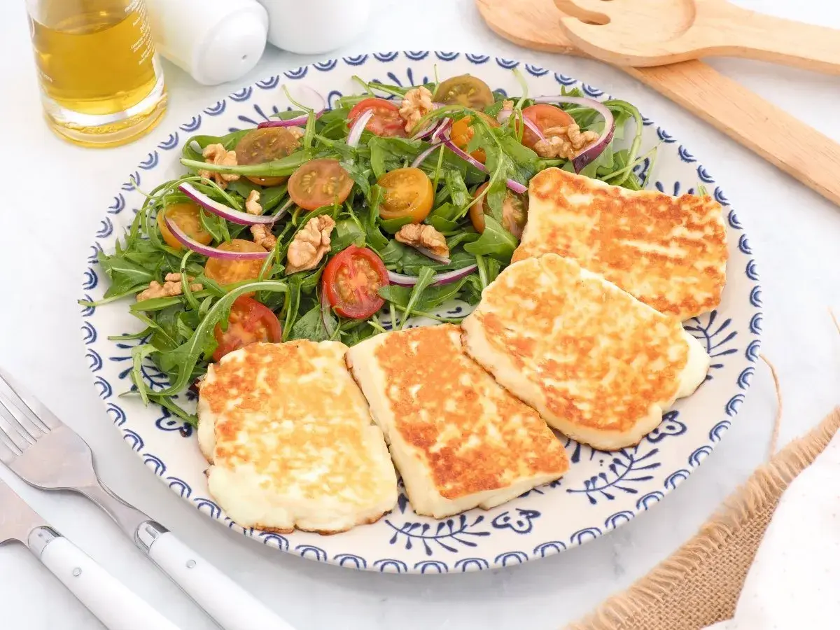 Ensalada fresca con tomates cherry, cebolla morada y nueces, acompañada de trozos dorados de ser halloumi a la plancha.