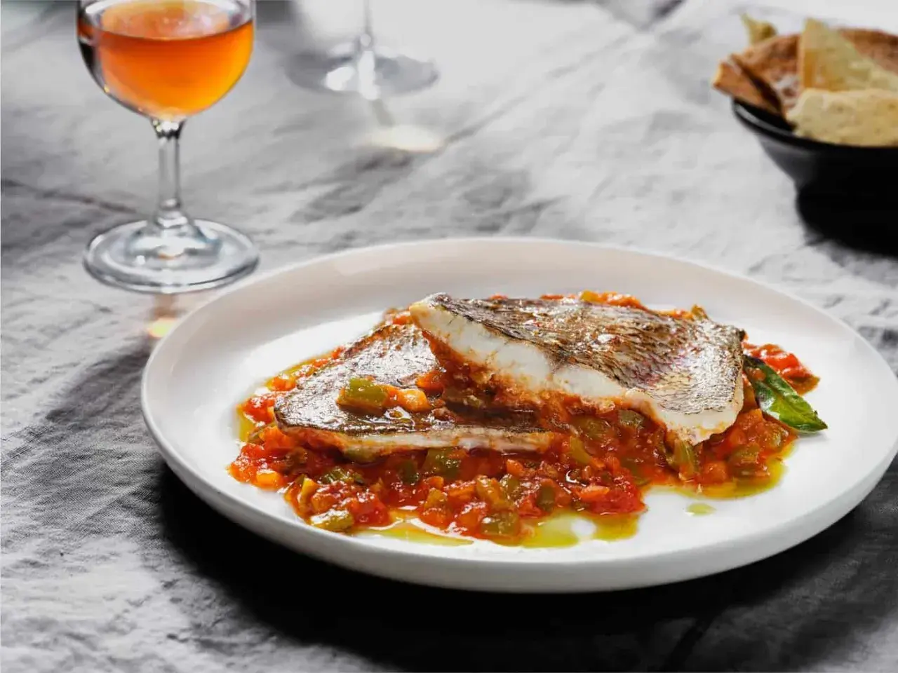 Deliciosa urta a la roteña servida en plato blanco, con guarnición de pimientos y tomate. Acompañada de copa de vino y pan.