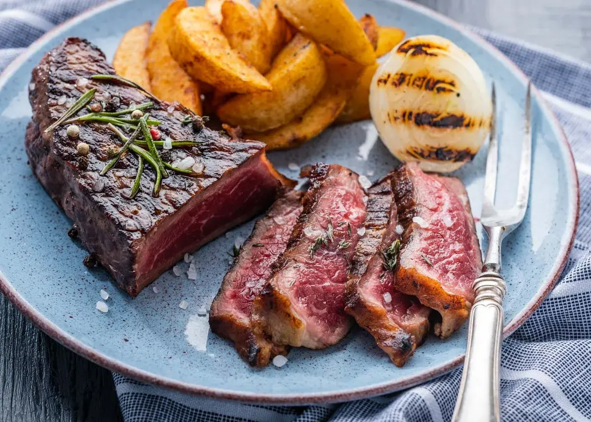 Jugoso entrecot a la plancha, cortado en rodajas, acompañado de patatas gajo y cebolla a la parrilla.