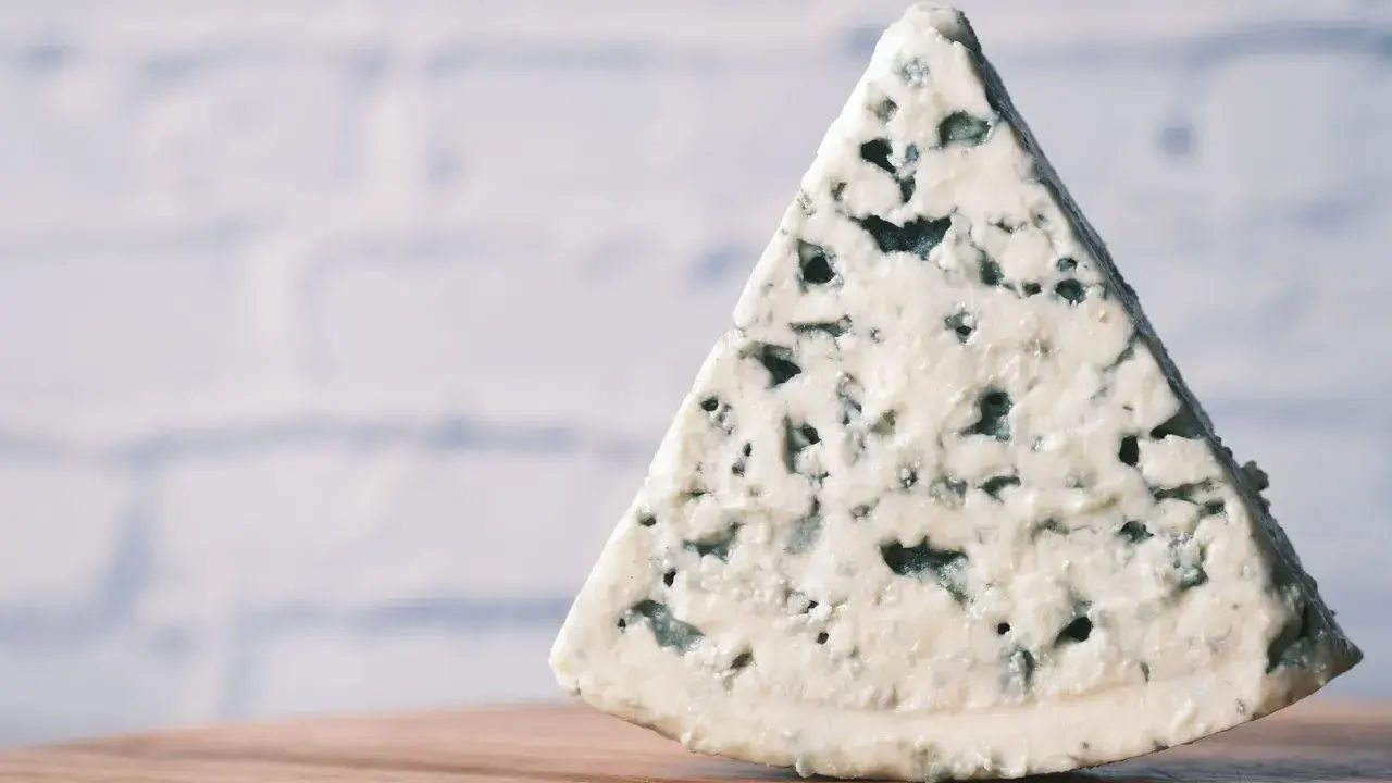 Un trozo triangular de queso azul, con sus características vetas de moho azul verdoso, descansa sobre una superficie de madera.