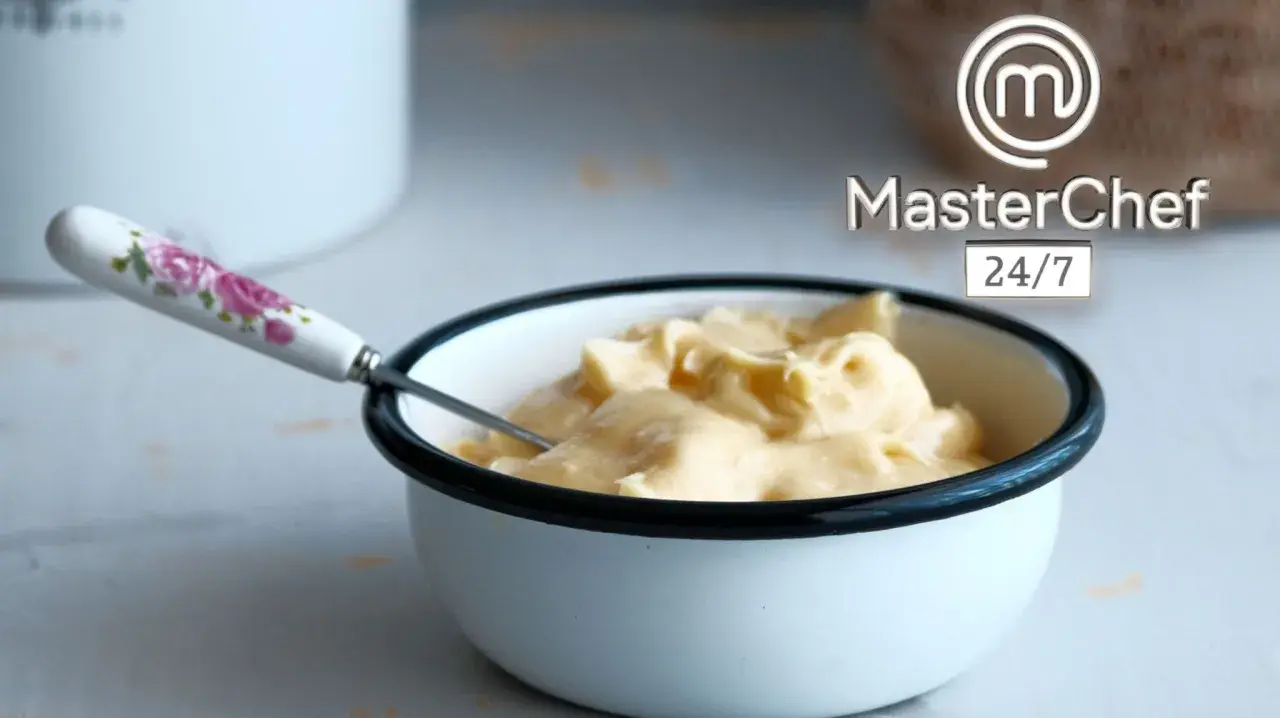 Crema sedosa lista para emulsionar en cocina. Un tazón blanco con borde negro contiene una suave crema amarilla, con una cuchara de mango floral.