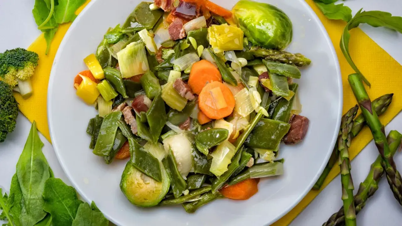 Un plato de menestra de verduras con judías verdes, zanahorias, puerros y trozos de jamón.