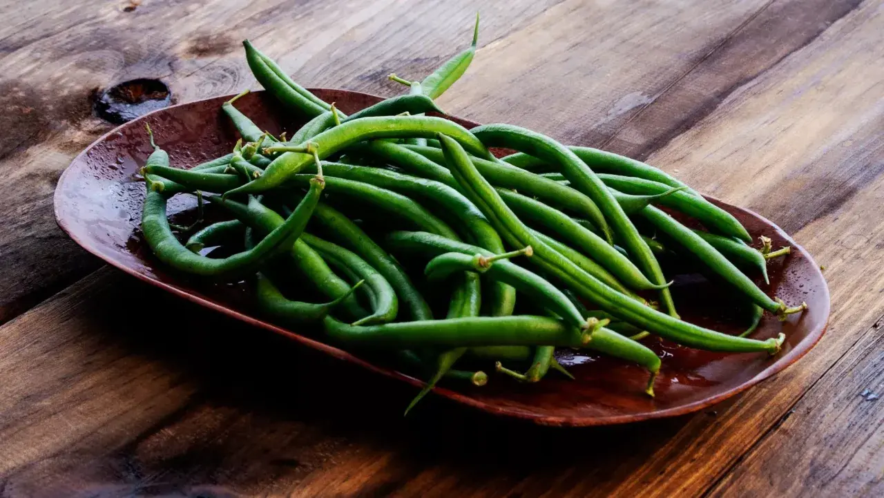Un plato de judías verdes frescas y vibrantes sobre una mesa de madera rústica, listas para ser cocinadas.