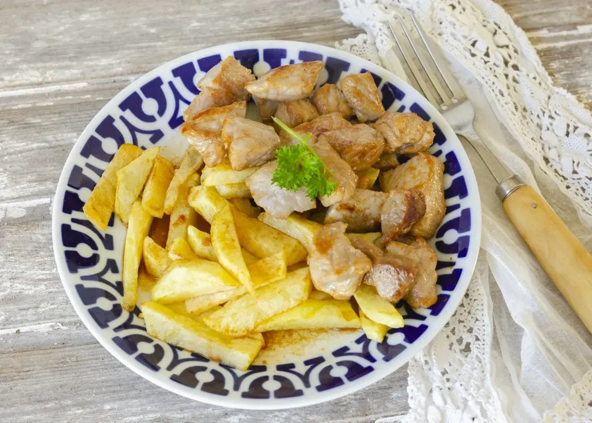 Raxo con patatas, un plato tradicional gallego, servido en un plato azul y blanco con perejil fresco.