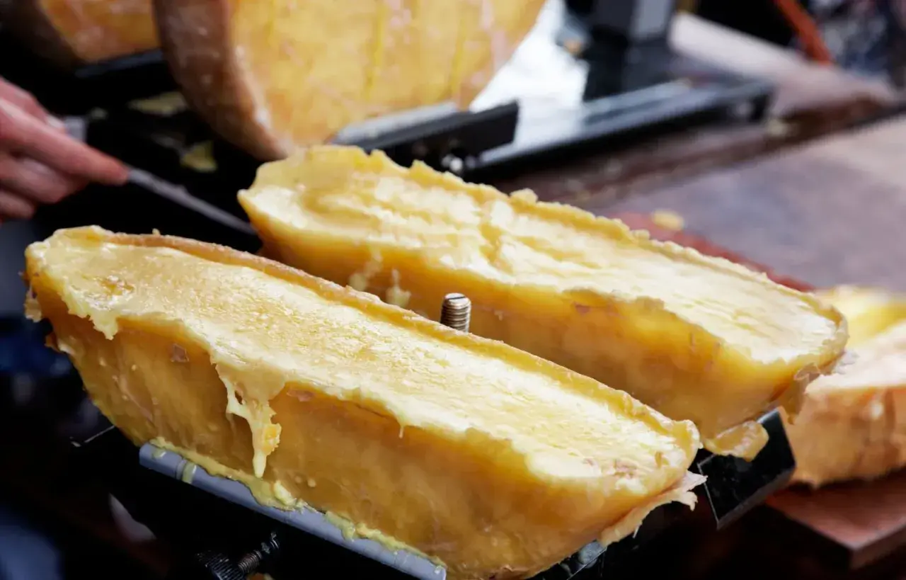 Dos mitades de queso fundido en una máquina para raclette, con el queso derritiéndose y goteando.