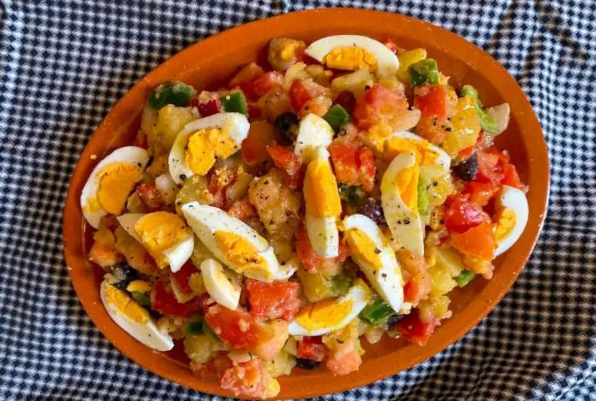 Ensalada campera con patatas, tomate, pimiento, aceitunas y huevos duros, servida en plato de barro.