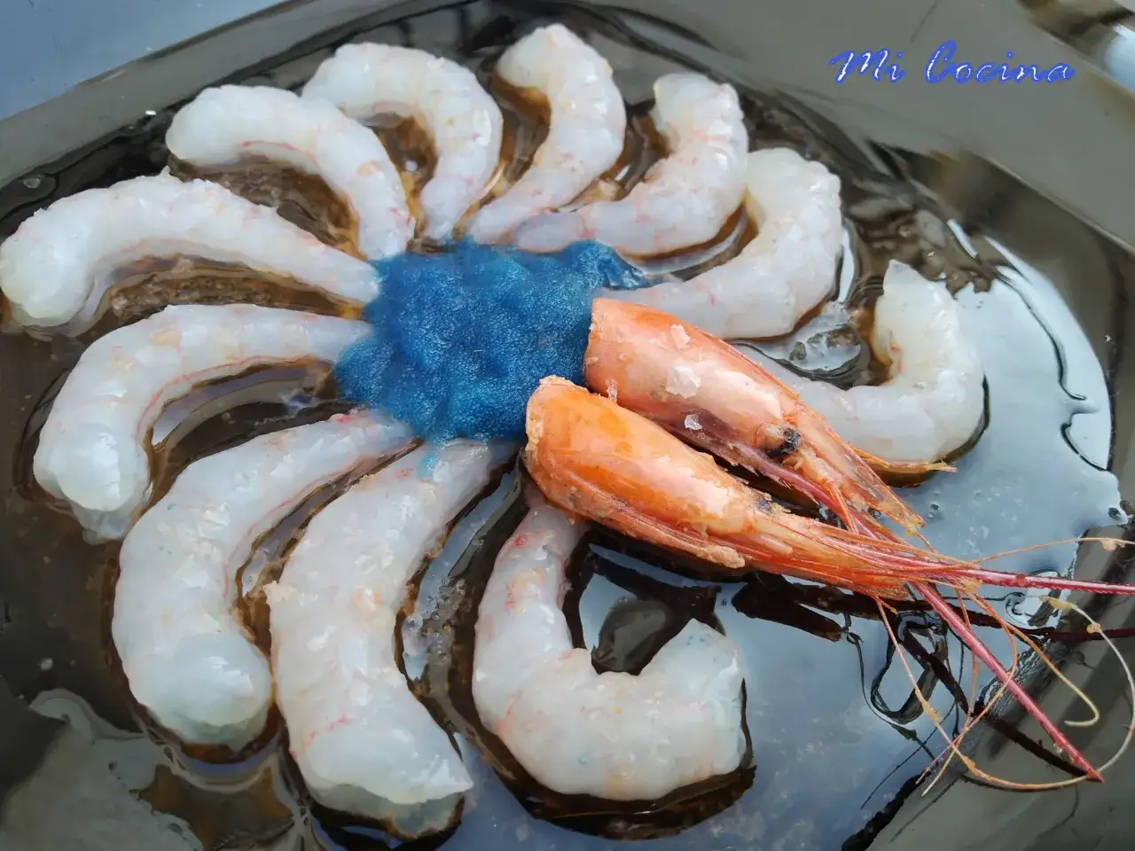 Gambas peladas dispuestas en círculo alrededor de una porción de huevas de gambas azules.