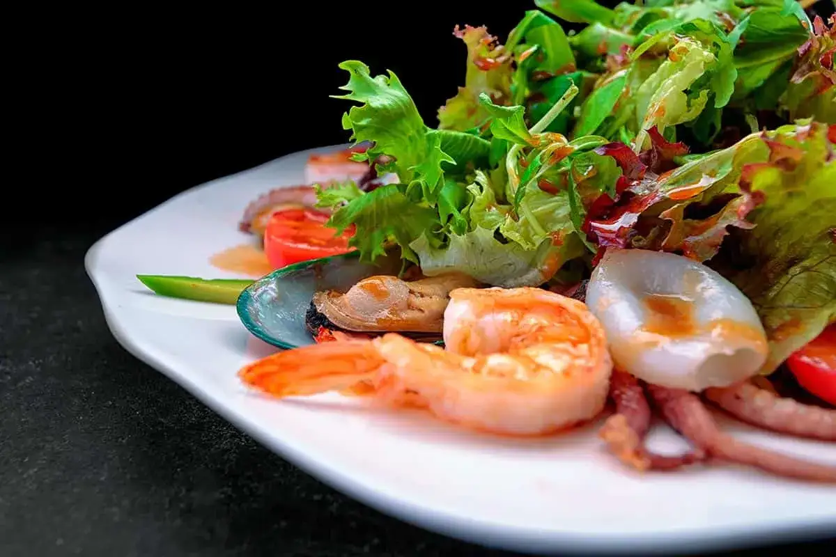 Deliciosa insalata di mare con gambas, mejillones, calamares y pulpo, servida con hojas verdes frescas y tomate.