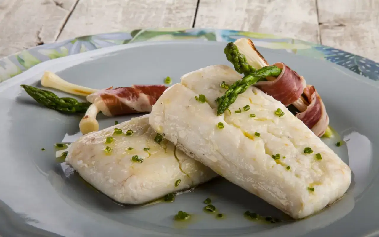 Deliciosa merluza confitada con esp&aacute;rragos y jam&oacute;n serrano, adornada con cebollino picado.