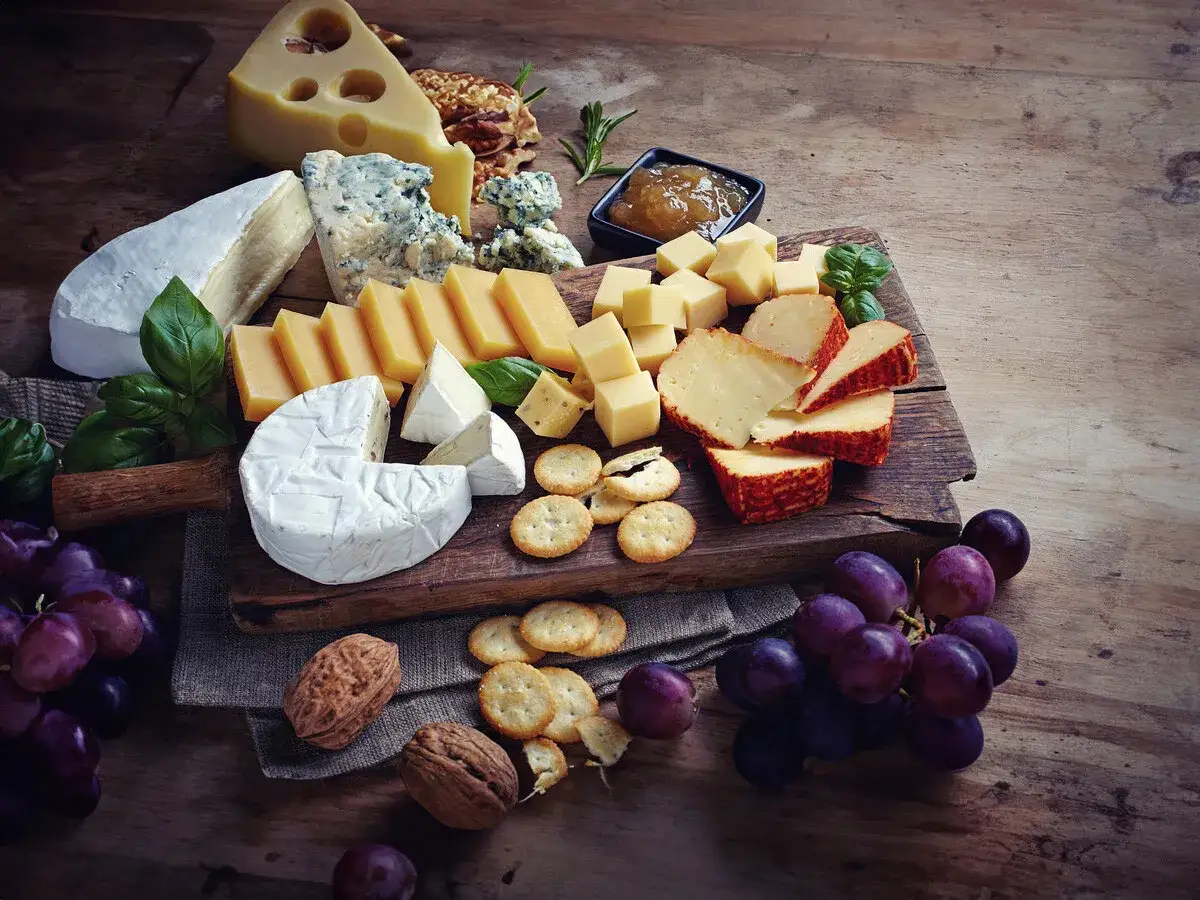 Tabla de quesos variados, incluyendo queso brie, con uvas, nueces y galletas. Ideal para acompañar con mermelada.