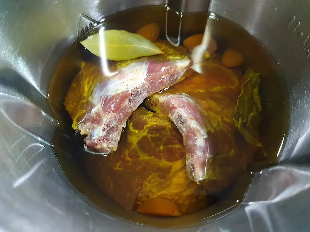 Carne cruda con hierbas y ajos sumergida en aceite, lista para confitar.