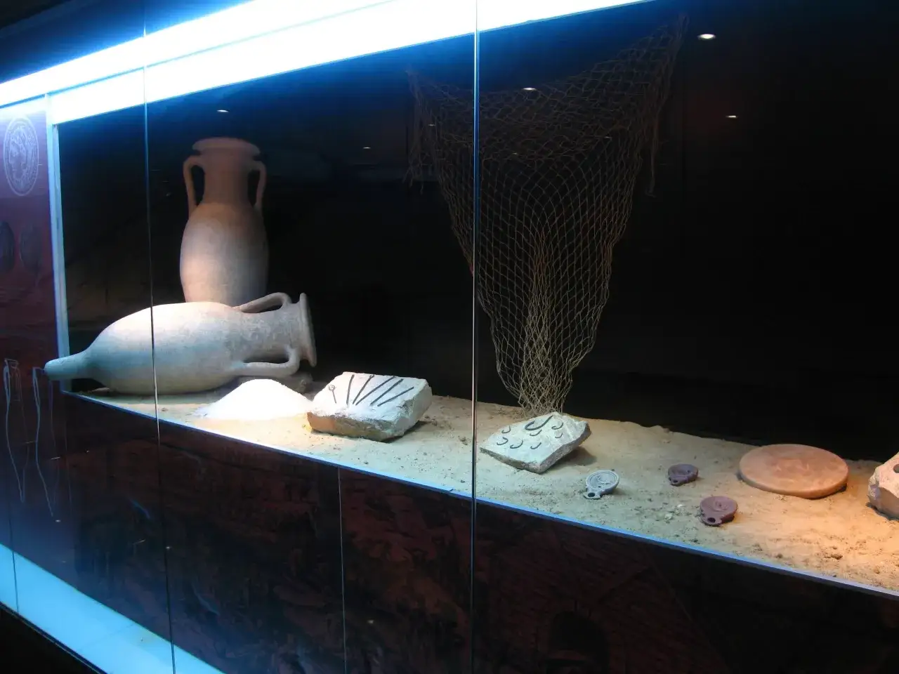 Exhibici&oacute;n de &aacute;nforas antiguas y una red de pesca, sugiriendo la producci&oacute;n y comercio de garum que es.