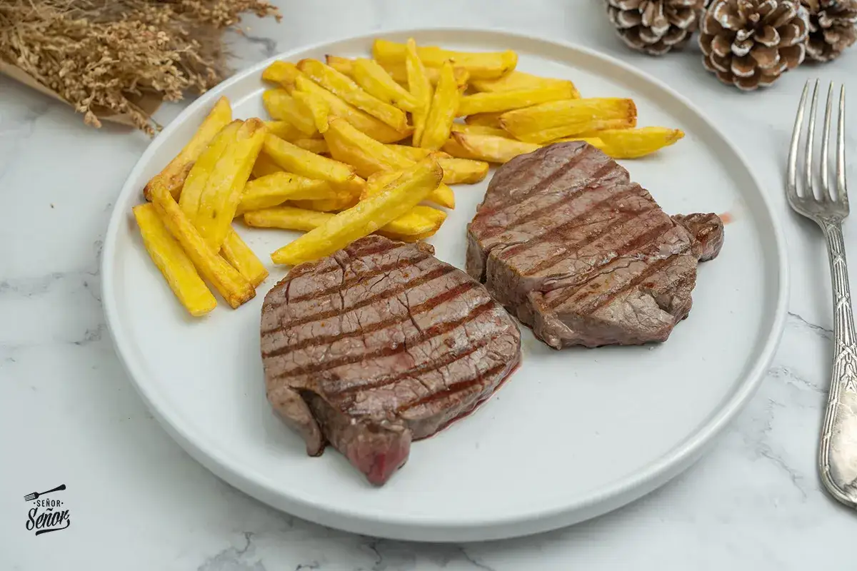 Dos jugosos solomillos de ternera a la parrilla con patatas fritas doradas. Un plato perfecto para disfrutar.