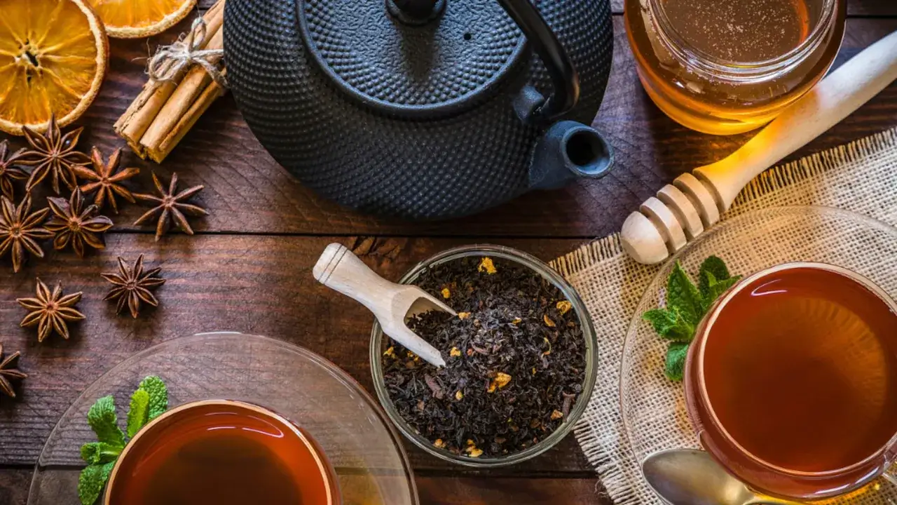 Una tetera negra, té negro suelto, tazas de té, miel y especias. Descubre a que sabe el té negro con estos ingredientes.