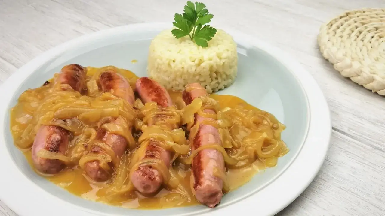 Salchichas al vino con cebolla caramelizada y una porción de arroz blanco, decorado con perejil.