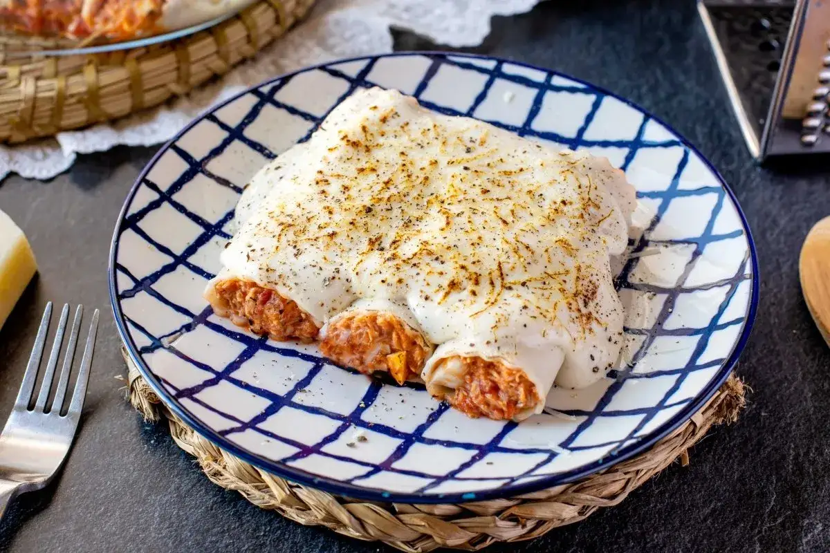 Canelones de atún gratinados con bechamel y queso, servidos en un plato con diseño de cuadros azules.