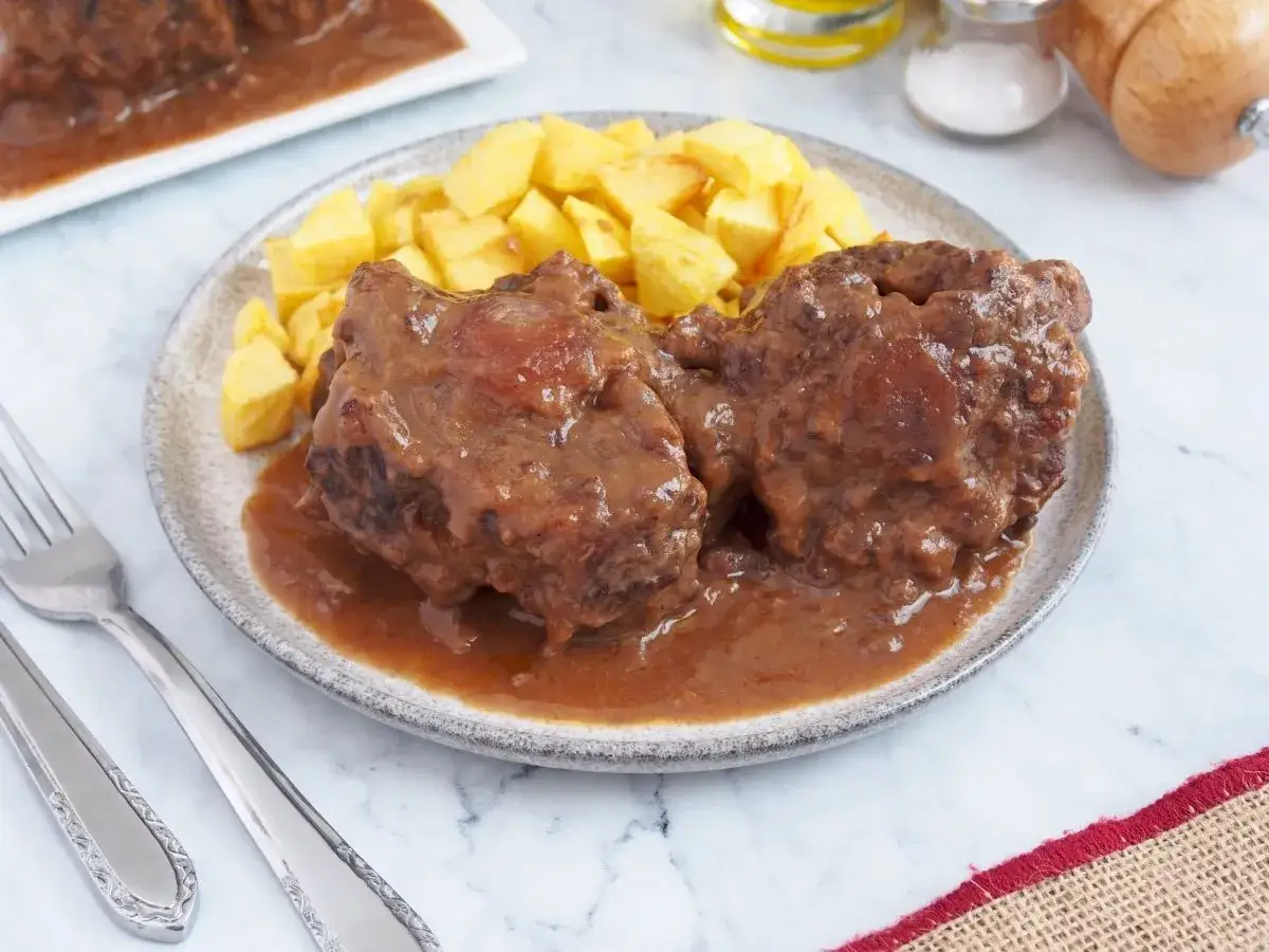 Dos trozos de rabo de toro en salsa, acompañados de patatas fritas. Un plato tradicional listo para disfrutar.