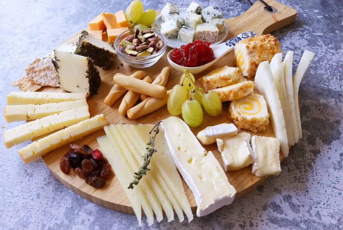 Tabla de quesos variados, con diferentes cortes para tablas: curados, frescos, azules y con hierbas. Acompañan uvas, frutos secos y mermelada.