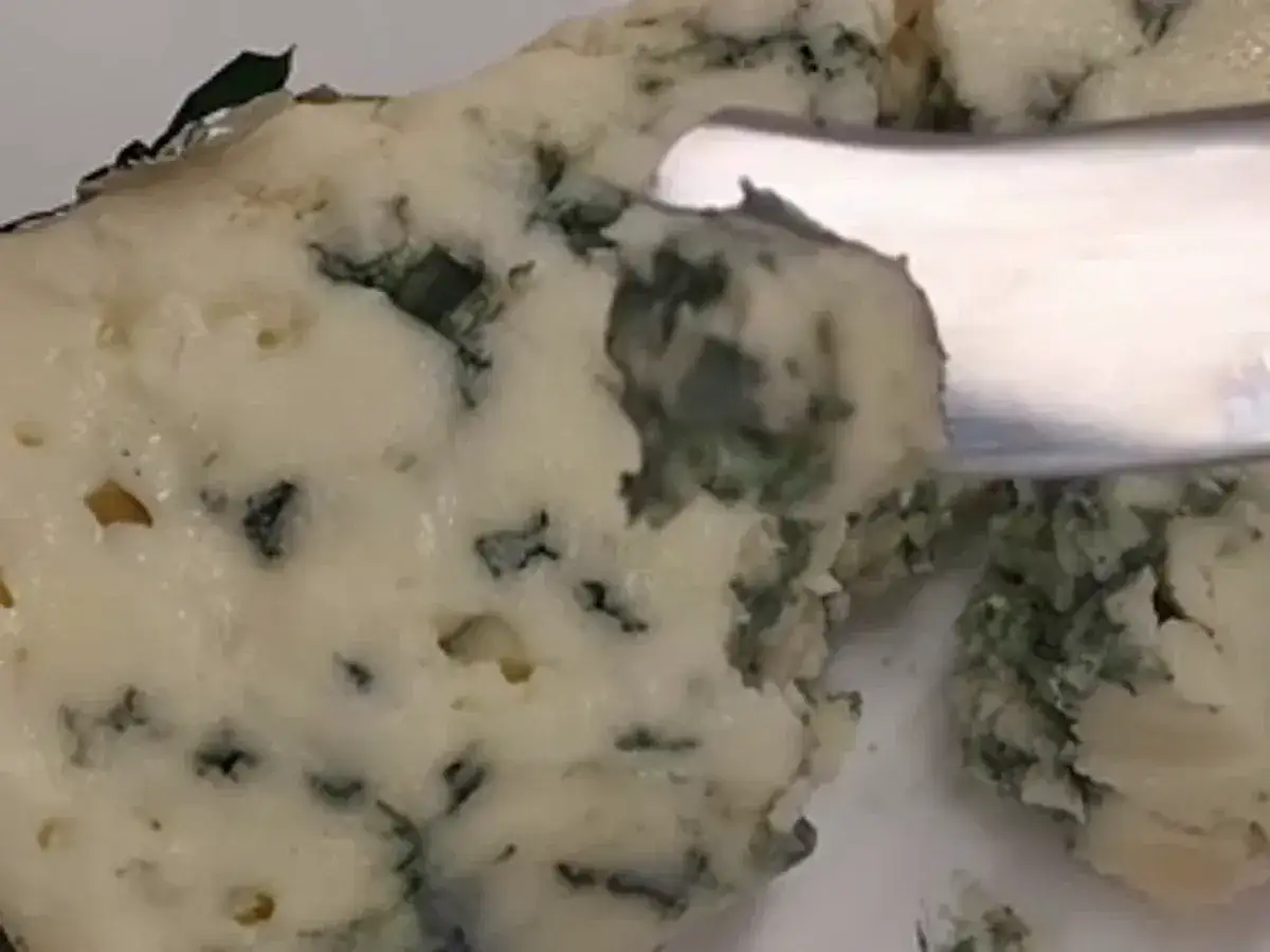 Un trozo de queso azul con vetas verdes y azules, indicando que el queso azul tiene moho. Un cuchillo corta un pedazo.