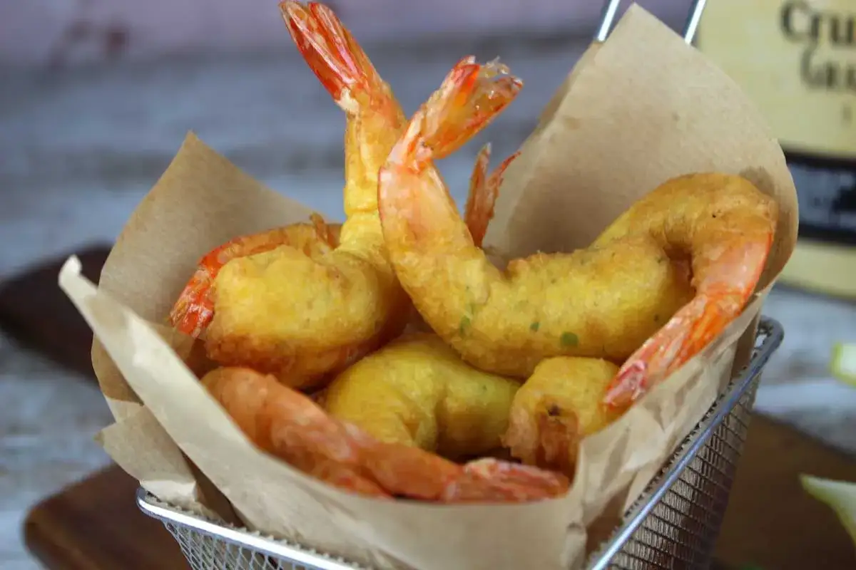 Crujientes gambas a la gabardina doradas y sabrosas, servidas en una cesta met&aacute;lica con papel de estraza.