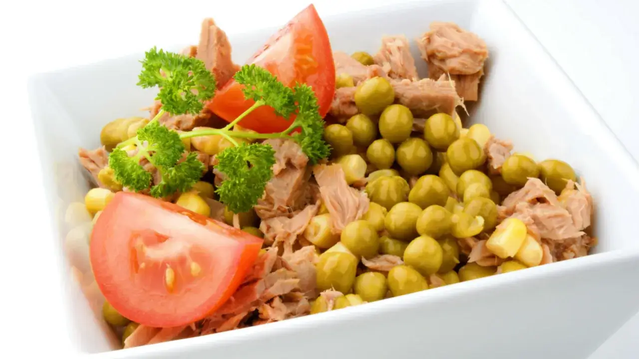 Ensalada fresca de guisantes con atún, maíz y trozos de tomate, decorada con perejil.